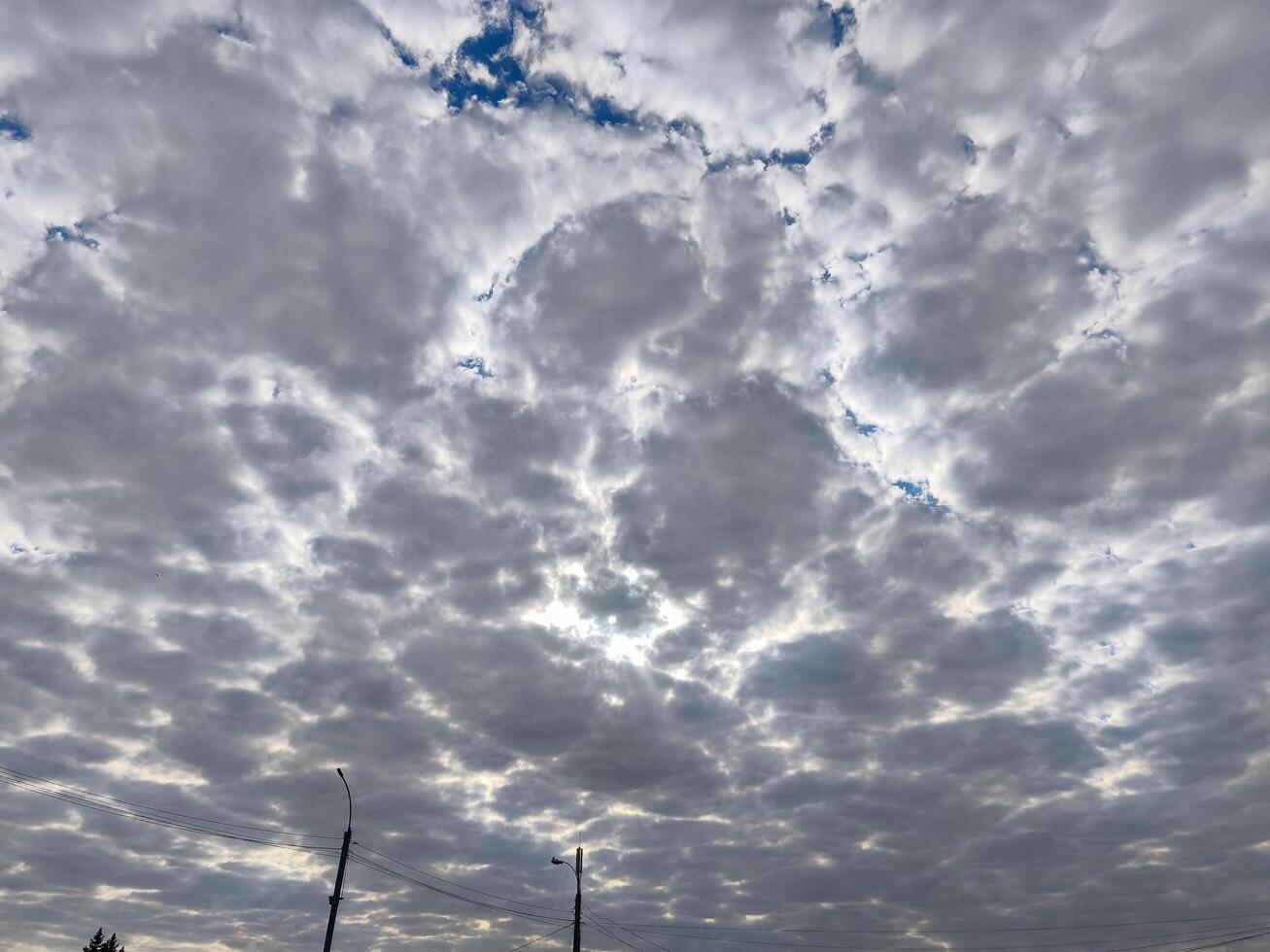 The sky is filled with fluffy white clouds, and the sun is peeking through them, creating a beautiful and calming scene. The clouds are scattered throughout the sky, with some closer to the ground photo