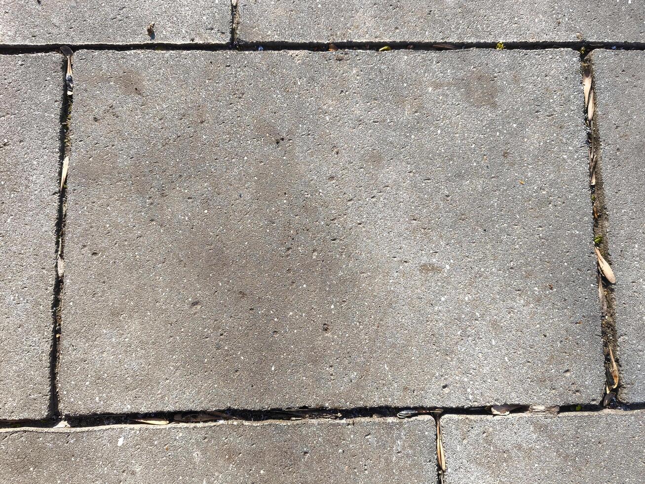 A gray stone sidewalk with a few cracks. The cracks are visible in the middle of the sidewalk photo