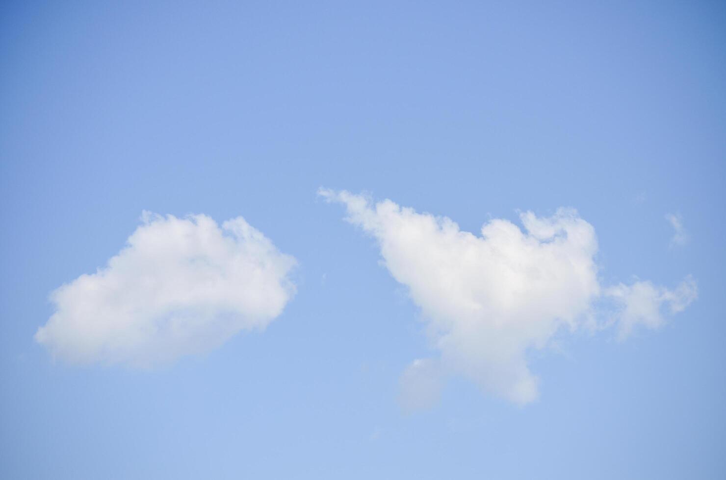 Two clouds in the sky, one is white and the other is grey. The sky is clear and blue photo