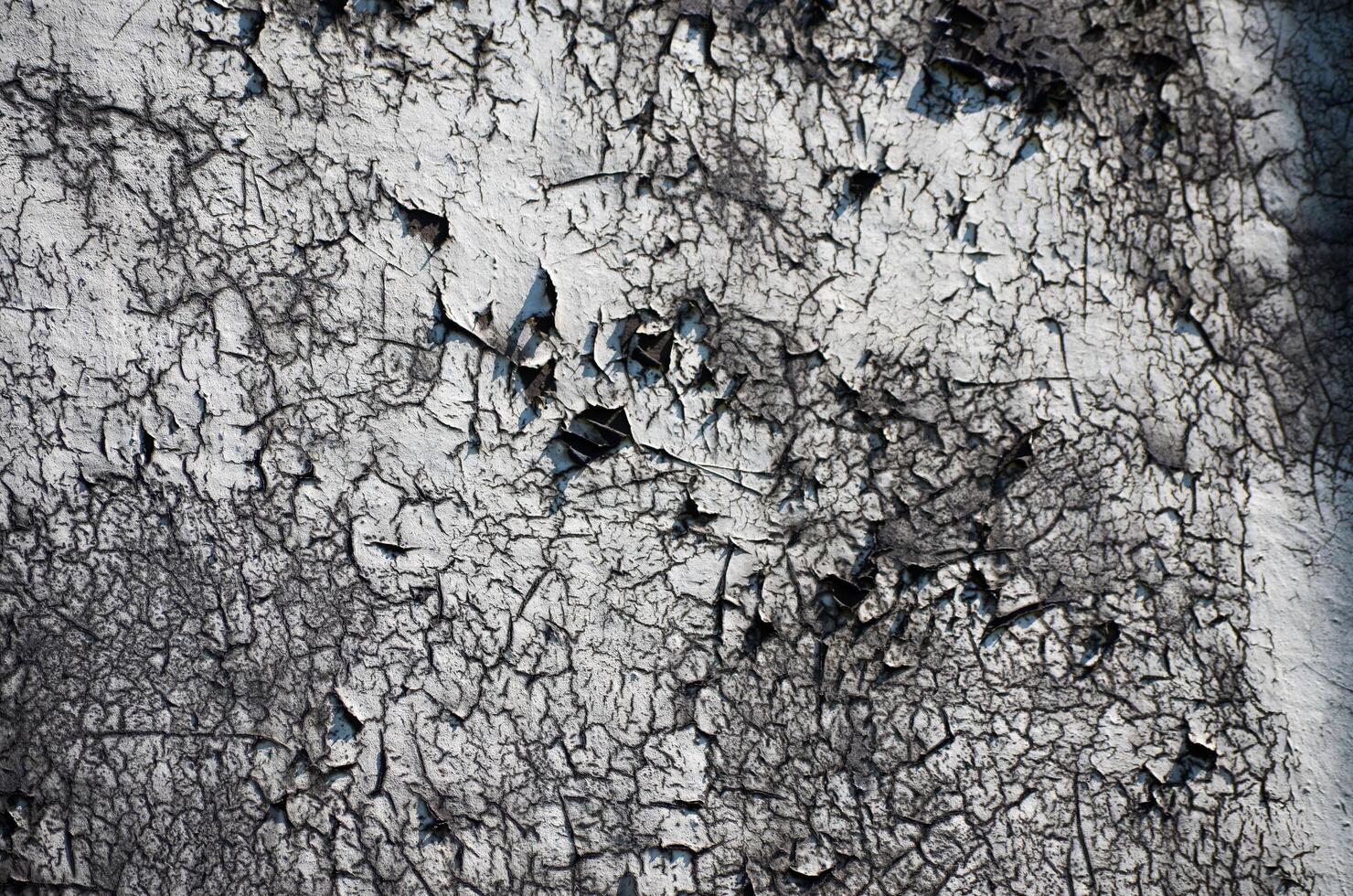 A wall with a lot of holes and cracks. The wall is gray and white. The cracks are deep and the holes are large photo