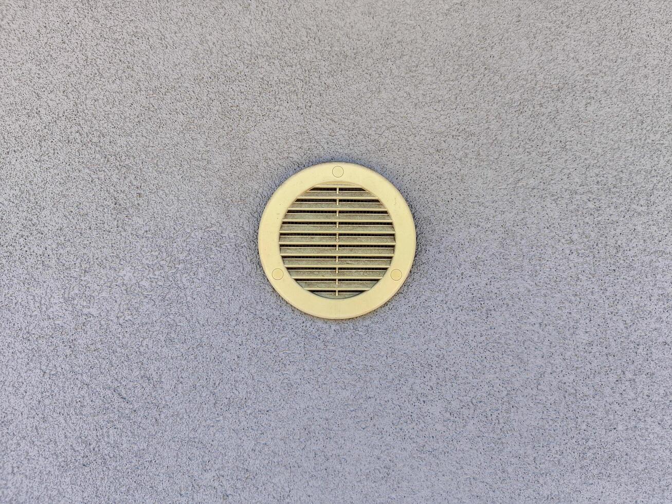 A vent is on the wall. It is yellow and has a hole in the middle photo