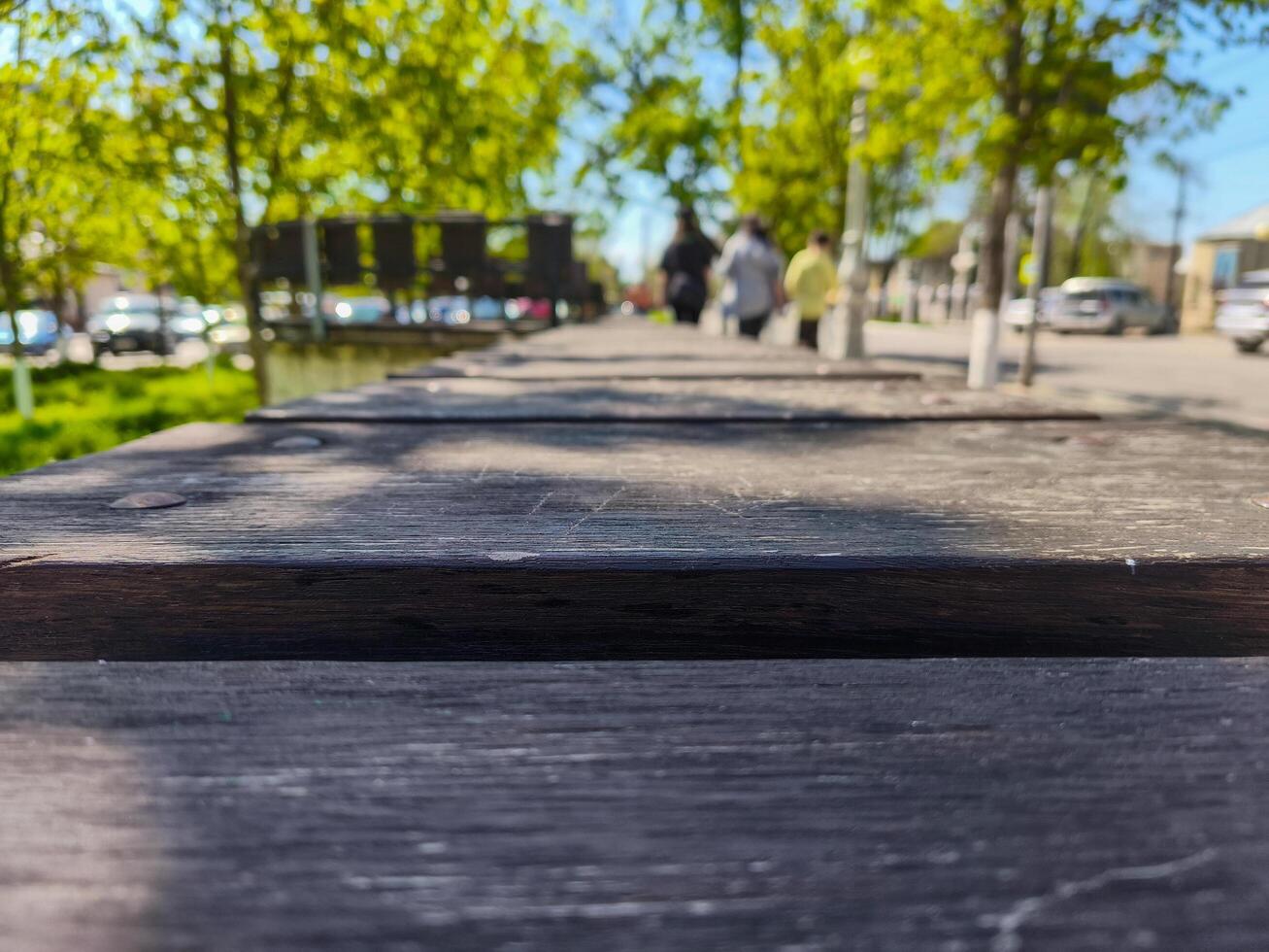 A wooden bench with a view of people walking by. The bench is empty photo