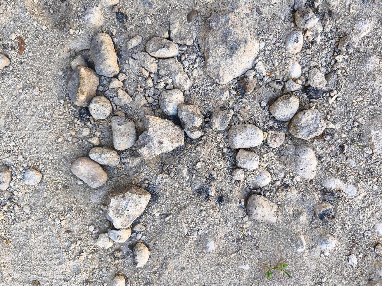 A pile of rocks on a sandy surface. The rocks are scattered and uneven, creating a rough and uneven texture. Concept of ruggedness and naturalness, as if the rocks have been left there by the elements photo