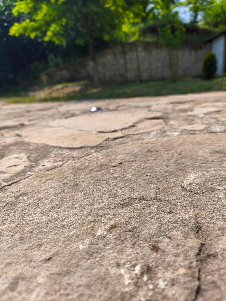 A close up of a stone walkway with a small object on it. The stone walkway is cracked and worn, giving it a sense of age and history. The small object on the ground is a silver coin photo