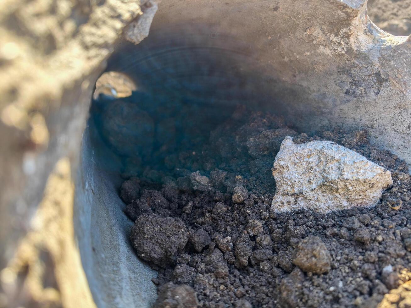 A hole in the ground with a rock in it. The hole is filled with dirt and rocks photo