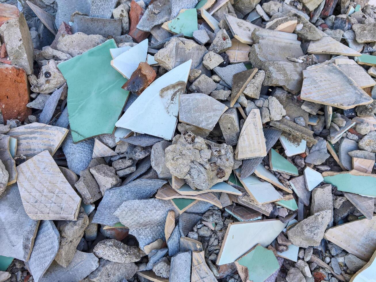 A pile of broken tiles and bricks. The pile is made up of many different sizes of tiles and bricks. The pile is scattered and disorganized photo