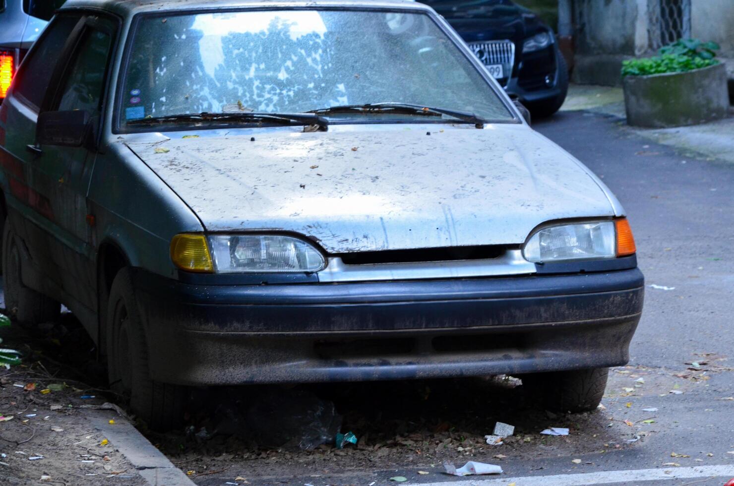 A dirty car is parked on the side of the road. The car is covered in dirt and has a few stickers on it. Scene is somewhat sad and neglected photo