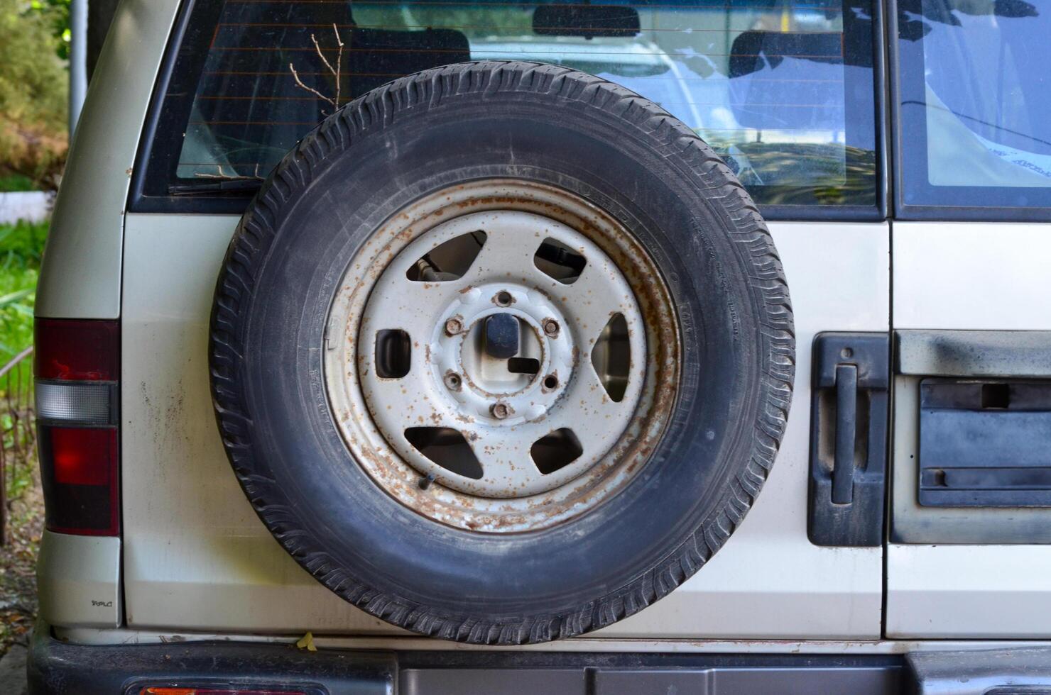 A white car with a black tire on the back. The tire is old and worn. The car is parked in a driveway photo