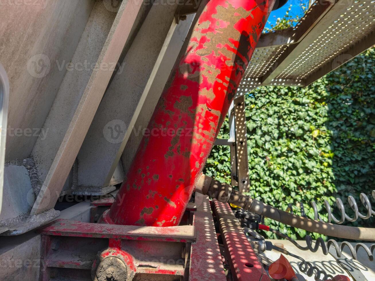 A red hydraulic cylinder is sitting on a concrete slab. The cylinder is rusty and has a lot of dirt on it photo
