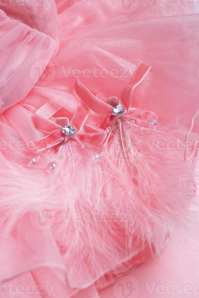 Close-up of soft pink fabric featuring velvet ribbon bows, sparkling gems, and delicate feathers. photo