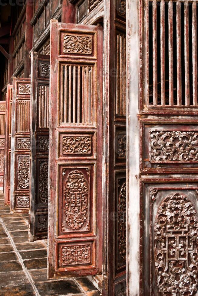 Intricately Carved Red Wooden Doors With Chinese Characters Partially Open To Reveal Interior Space. photo