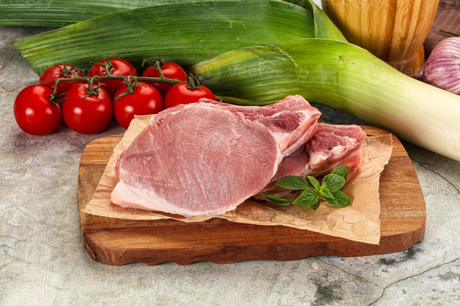 Raw pork on a cutting board with vegetables and tomatoes photo