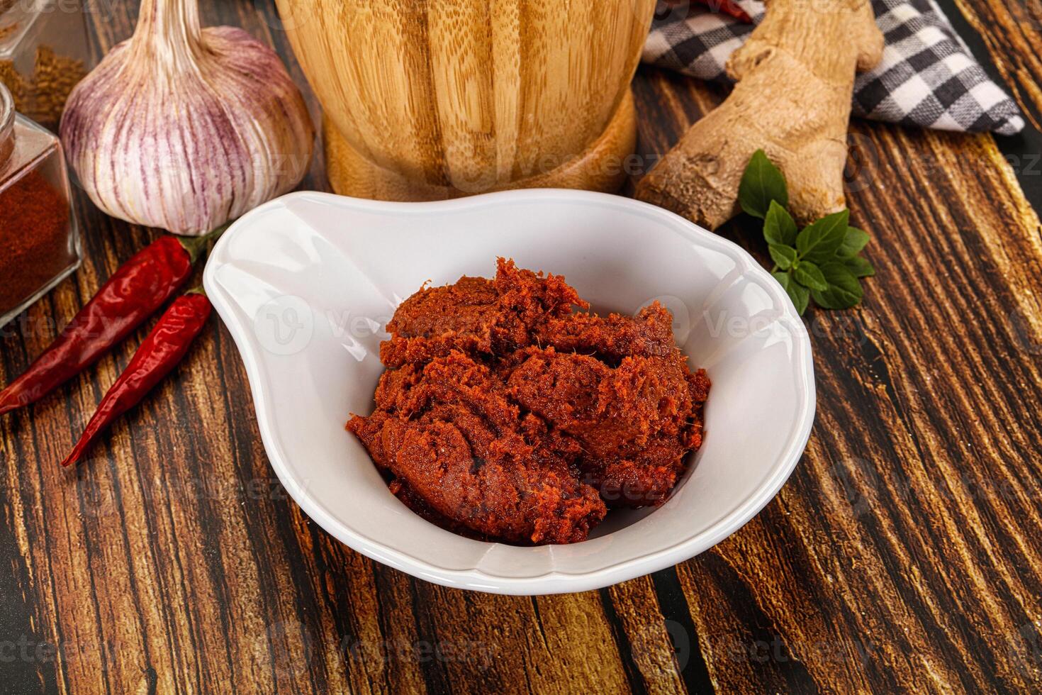 A bowl of red chili paste next to a bottle of garlic photo