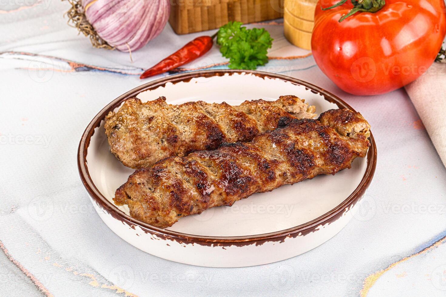 Two skewers of meat on a plate with a tomato and a knife photo