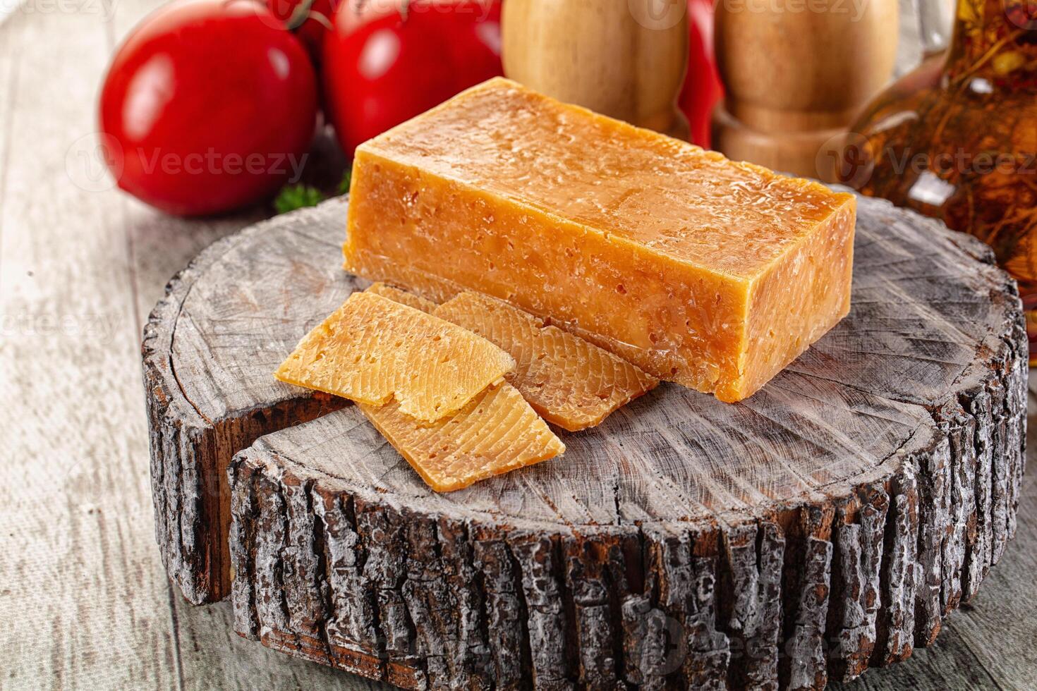 A piece of cheese on a wooden block with tomatoes and other vegetables photo