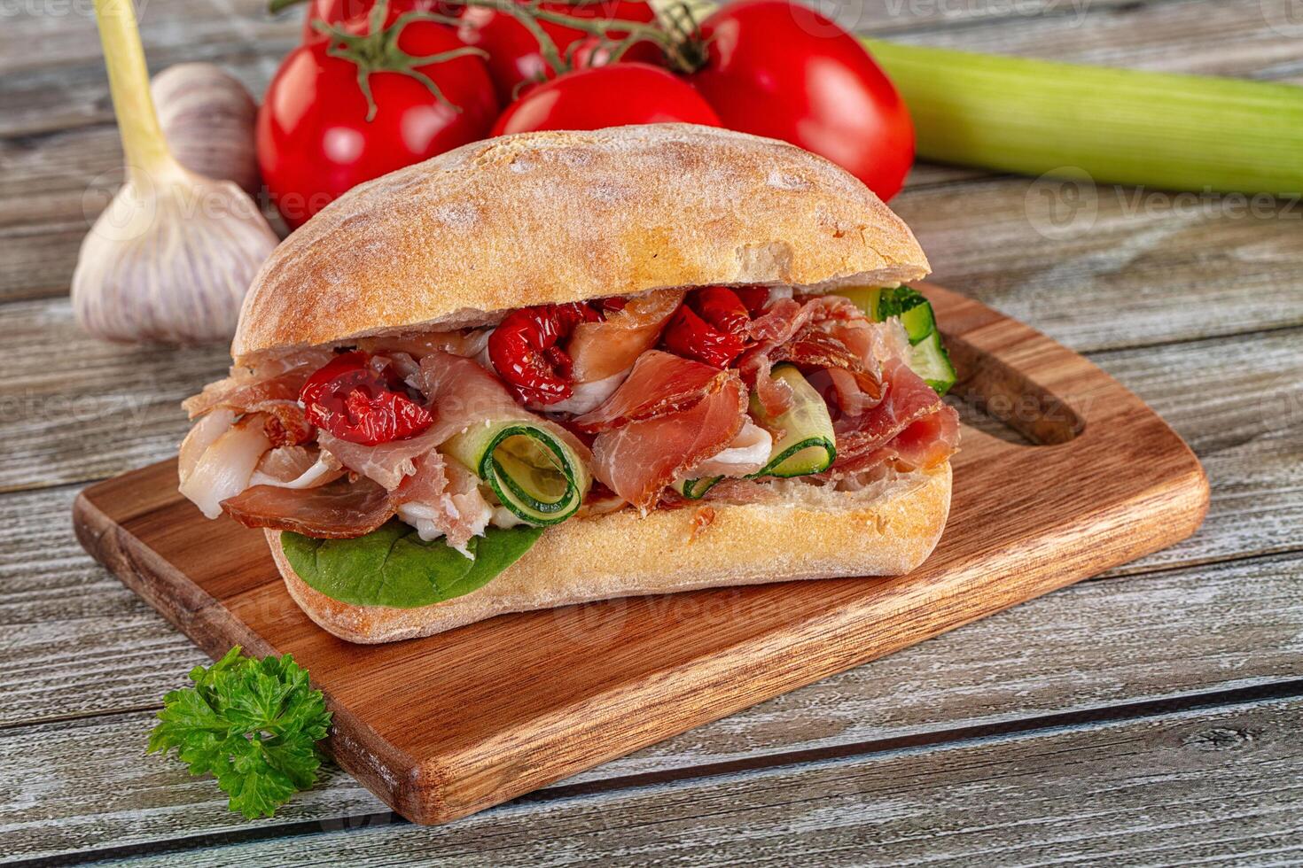A sandwich on a wooden cutting board with tomatoes and cucumbers photo