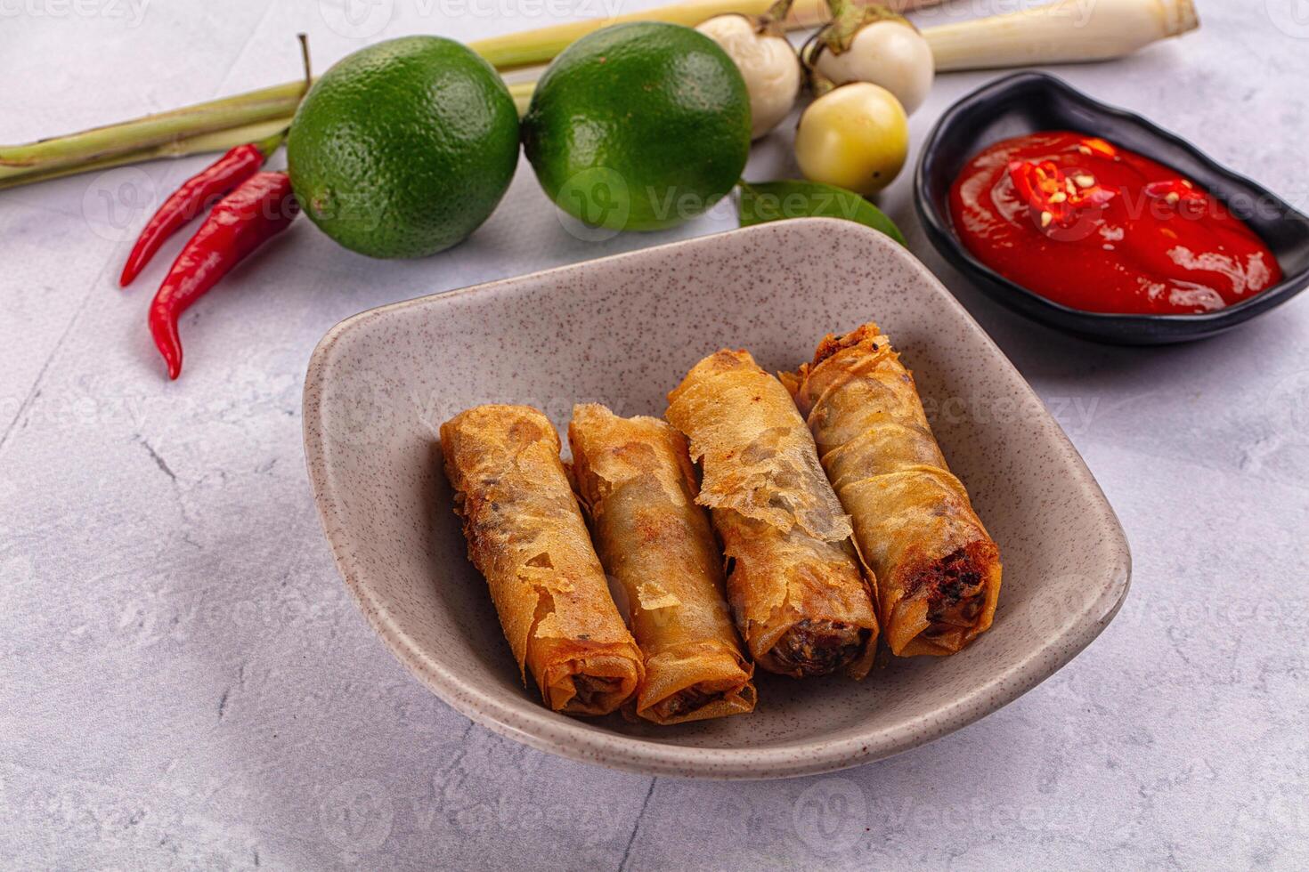 A bowl of spring rolls with a bowl of sauce and a bowl of chili peppers photo
