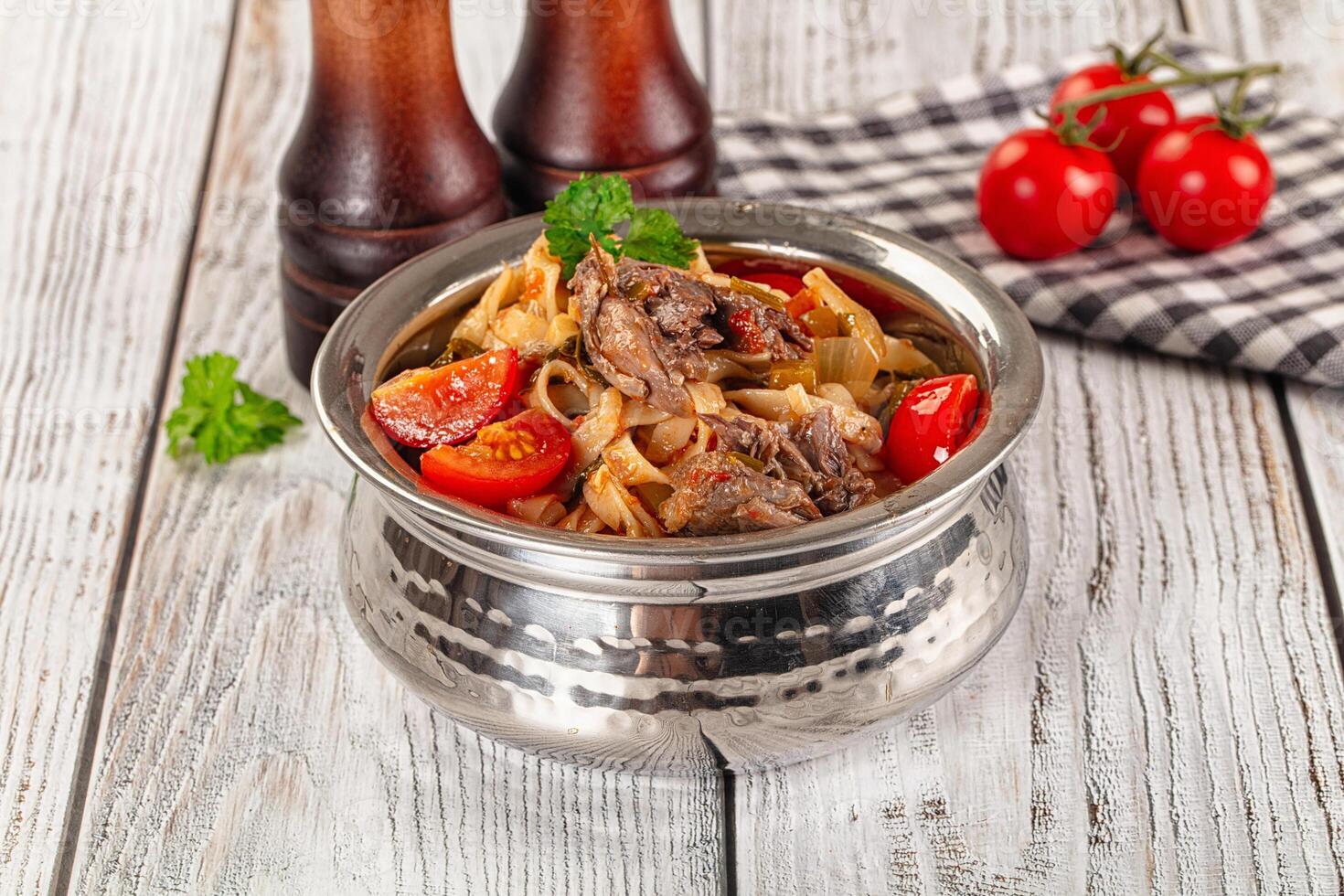 A bowl of meat and vegetables with tomatoes and a bottle of beer photo