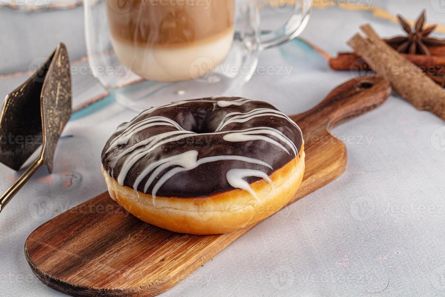 A donut on a wooden board with a cup of coffee and a spoon photo