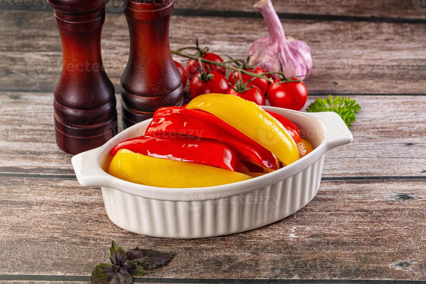 A white dish with peppers and garlic on a wooden table photo