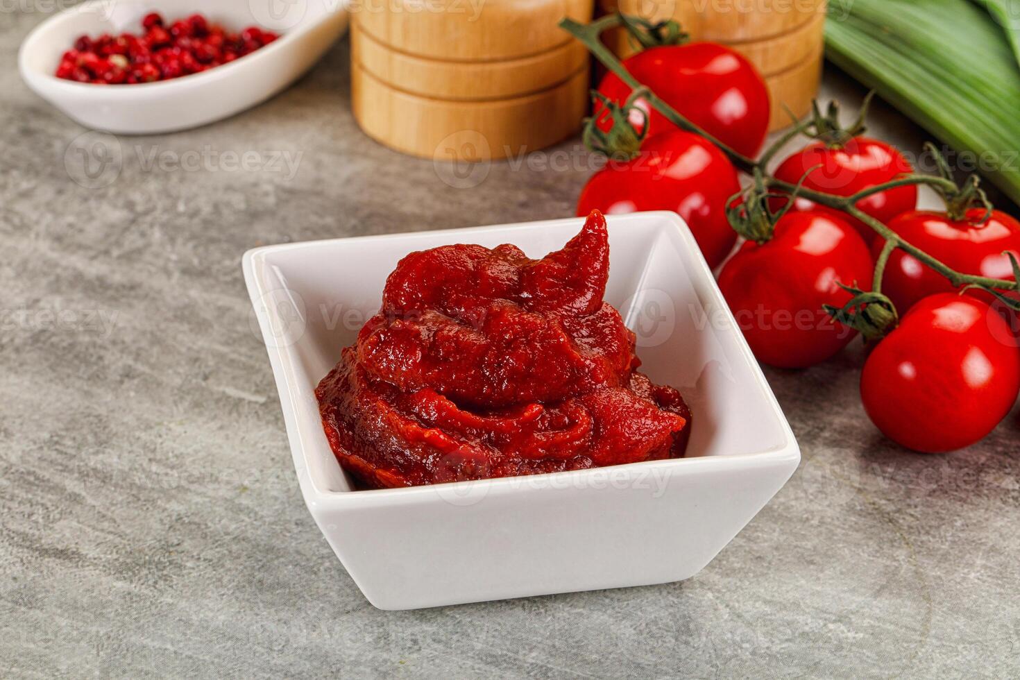 A bowl of red sauce next to a bowl of tomatoes photo