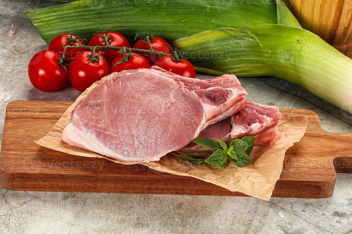 Raw pork on cutting board with tomatoes and vegetables photo