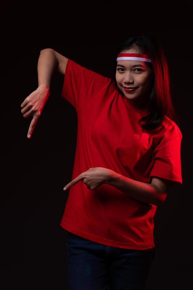 Portrait of Young Asian Woman Pointing Down Wearing Red Outfit, Indonesian Independence Day Concept Smiling photo