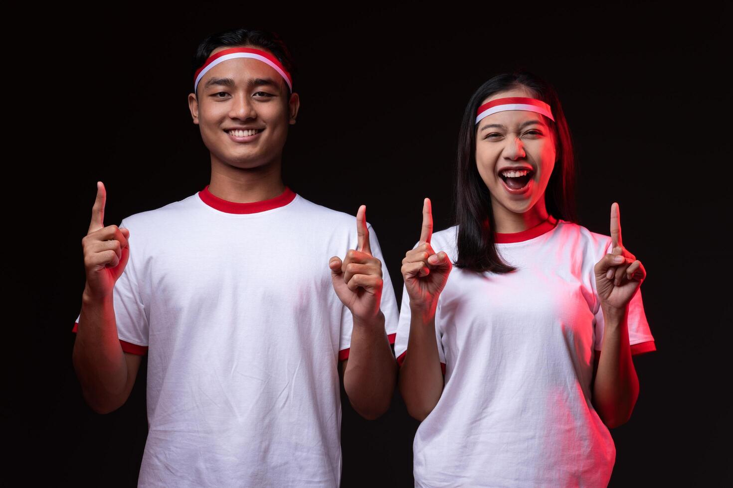 Portrait of Young Asian Man and Woman Pointing Up Wearing Red White Outfit, Indonesian Independence Day Concept photo