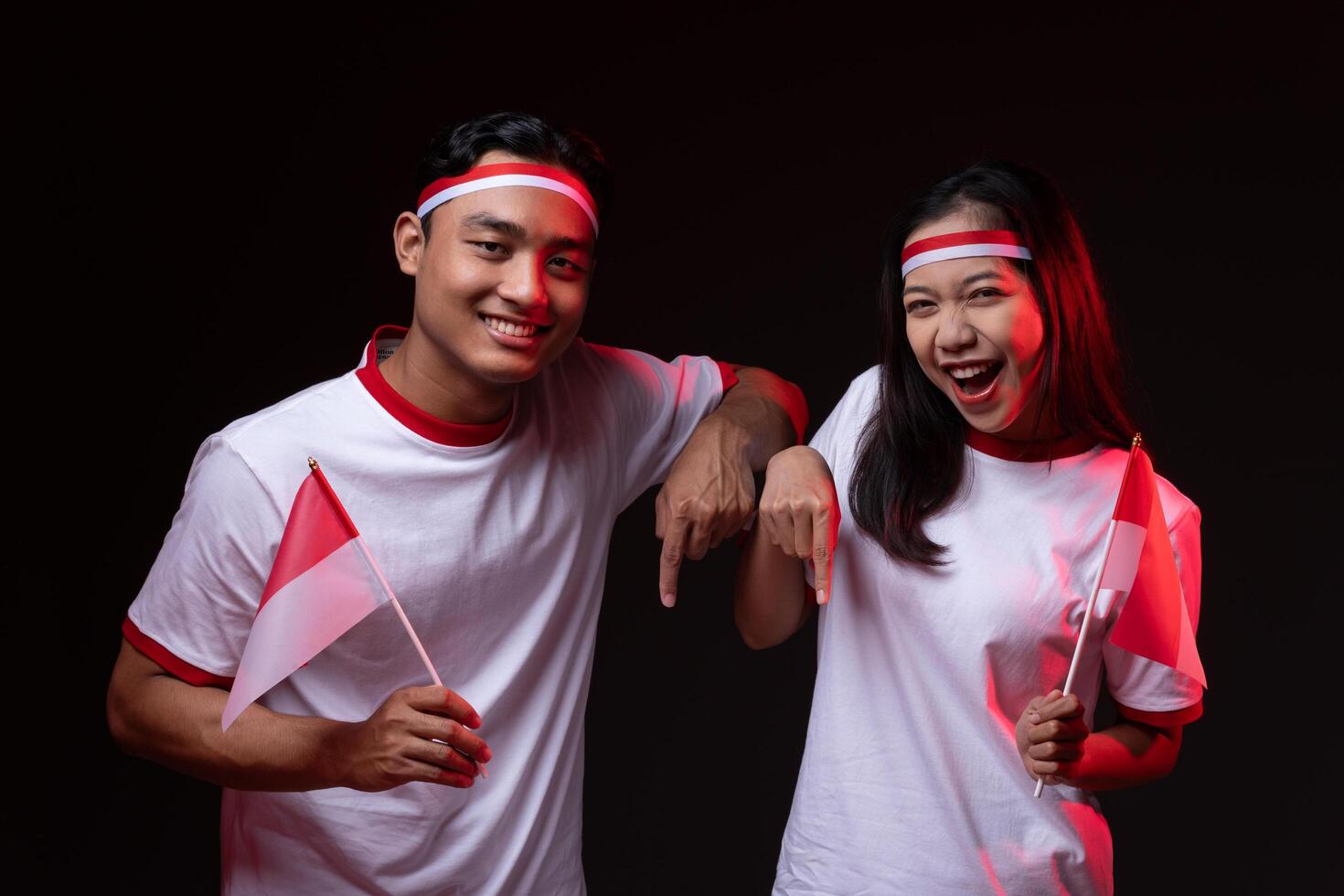 Portrait of Young Asian Man and Woman Pointing Down Wearing Red White Outfit, Indonesian Independence Day Concept Isolated Background photo