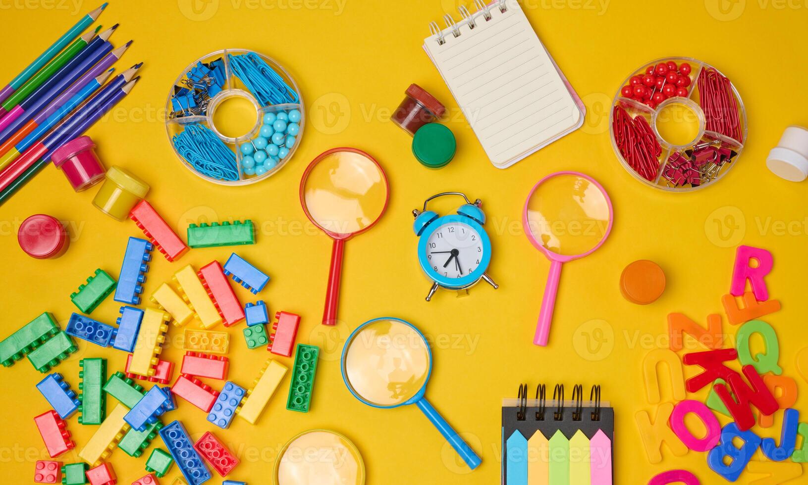 Collection of colorful school supplies, building bricks, letters, and learning items scattered on a yellow background. Play and education concept. photo