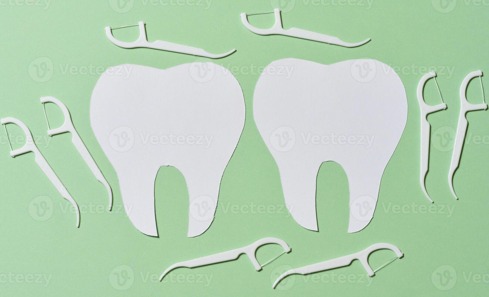 Two white paper cutouts of teeth are surrounded by multiple white dental floss picks on a light green background, emphasizing dental hygiene photo