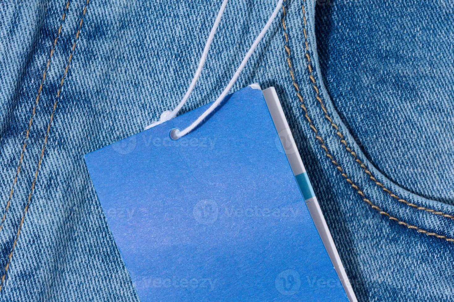 Light blue denim jeans with a blank blue price tag attached to the belt loop. photo
