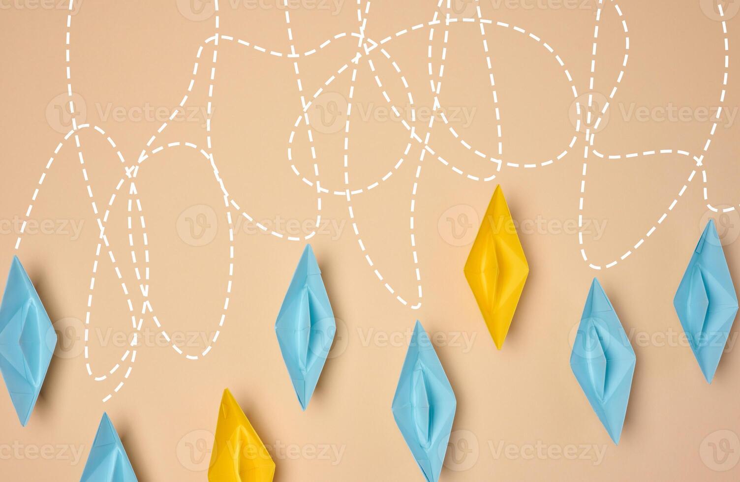 A creative composition featuring blue and yellow paper boats with dashed lines trailing behind them on a beige background, journey or exploration photo