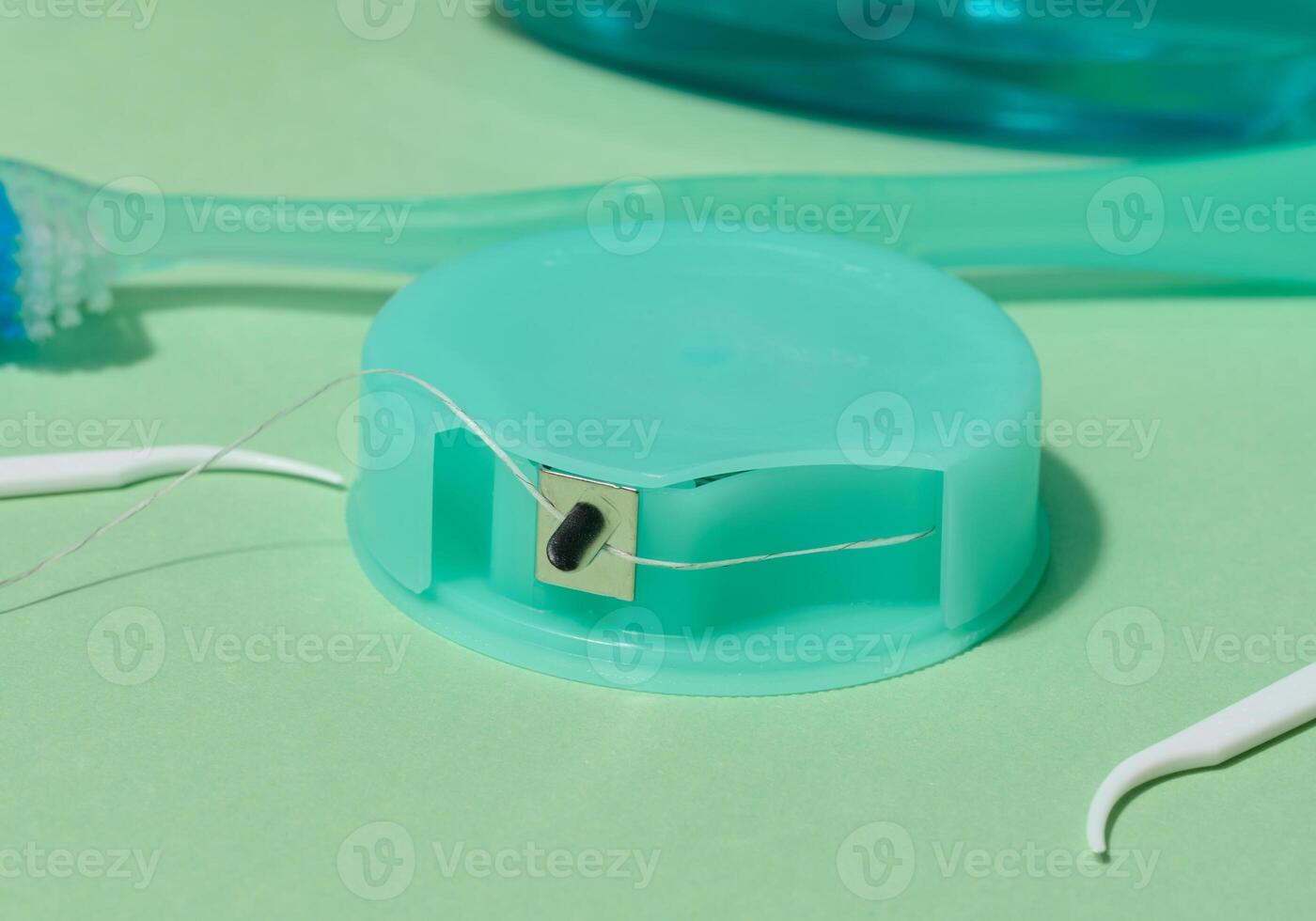 A turquoise dental floss container with floss extended, along with white floss picks, are shown on a light green background photo