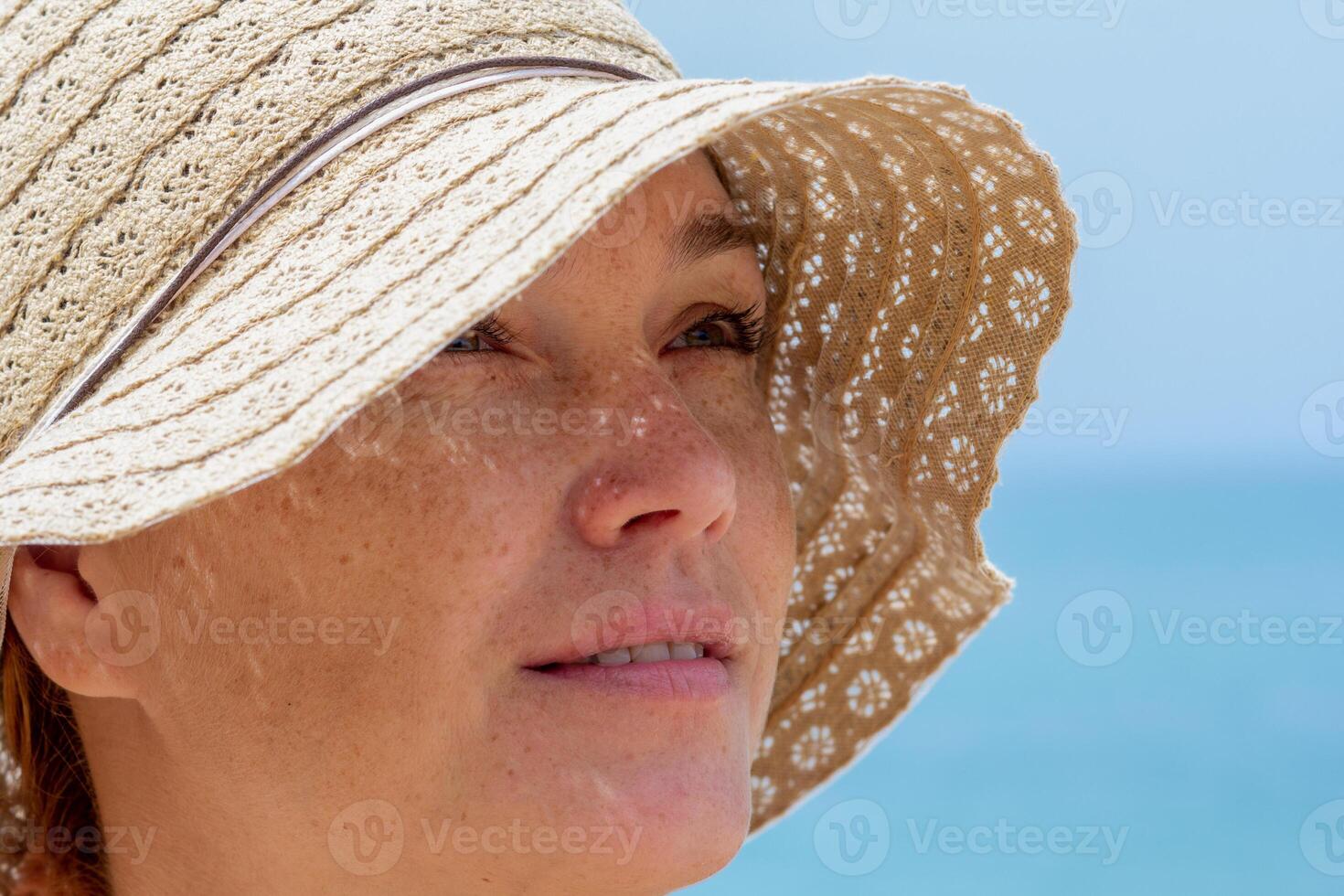 Close up caucasian middle aged woman face in sun hat looking aside over blue sea photo