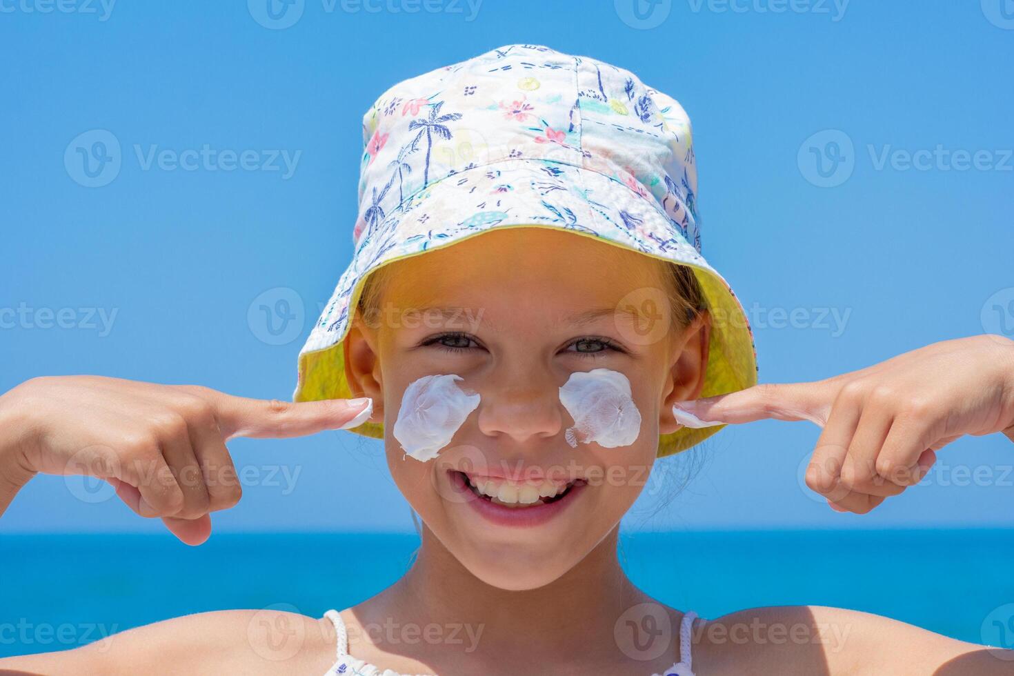 Caucasian smiling child of 8 9 years in a sun hat showing on sunscreen on cheeks over sea looking at camera photo