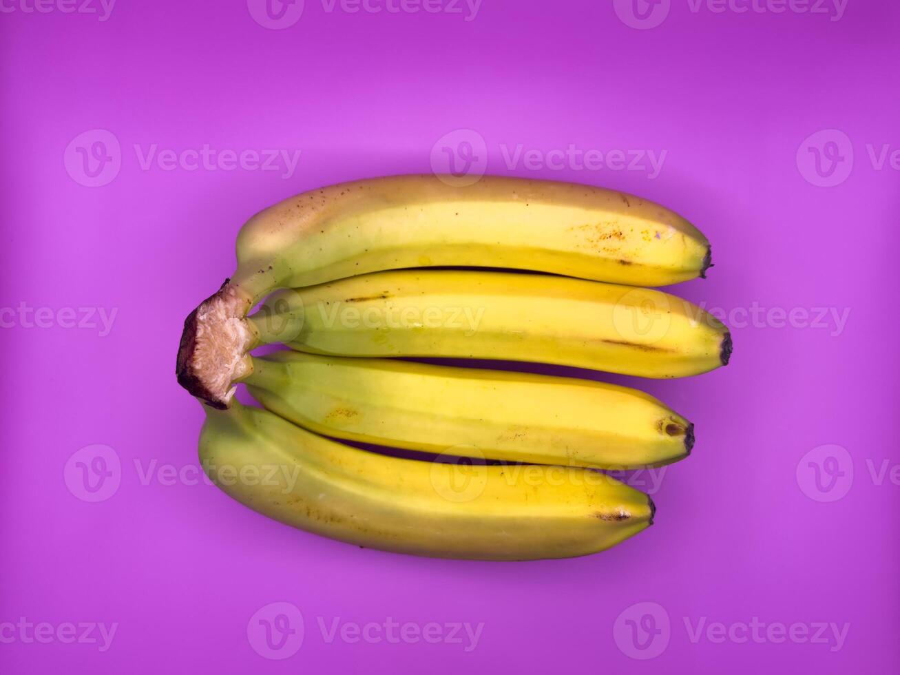 4 bright yellow bananas, uncut, lying next to each other on a bright purple background, top view photo