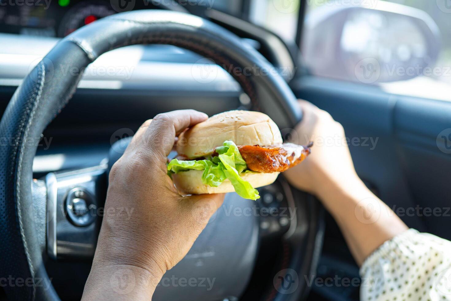 Asian woman driver hold and eat hamburger in car, dangerous and risk an accident. photo