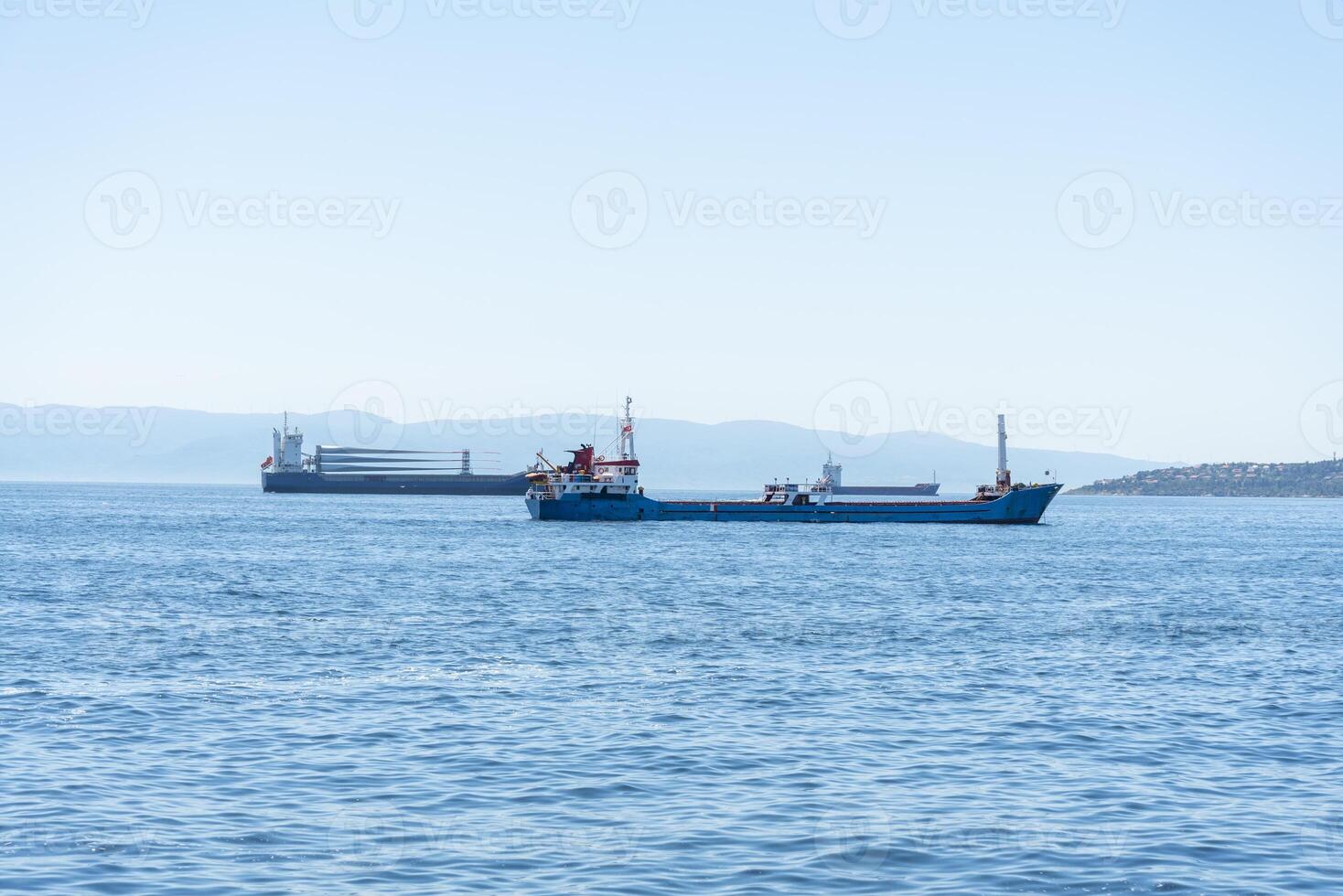 Cargo and container ships navigating calm waters near coastal hills under clear blue skies photo
