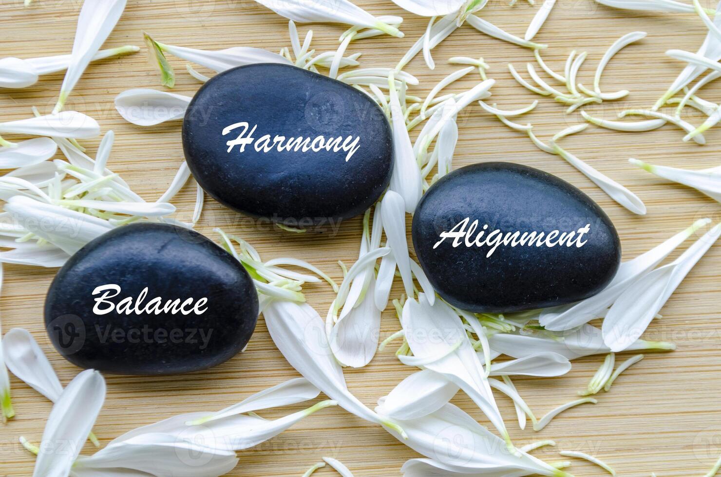 Balance, Harmony, and Alignment text on zen stones surrounded by flower petals. Inner peace concept photo