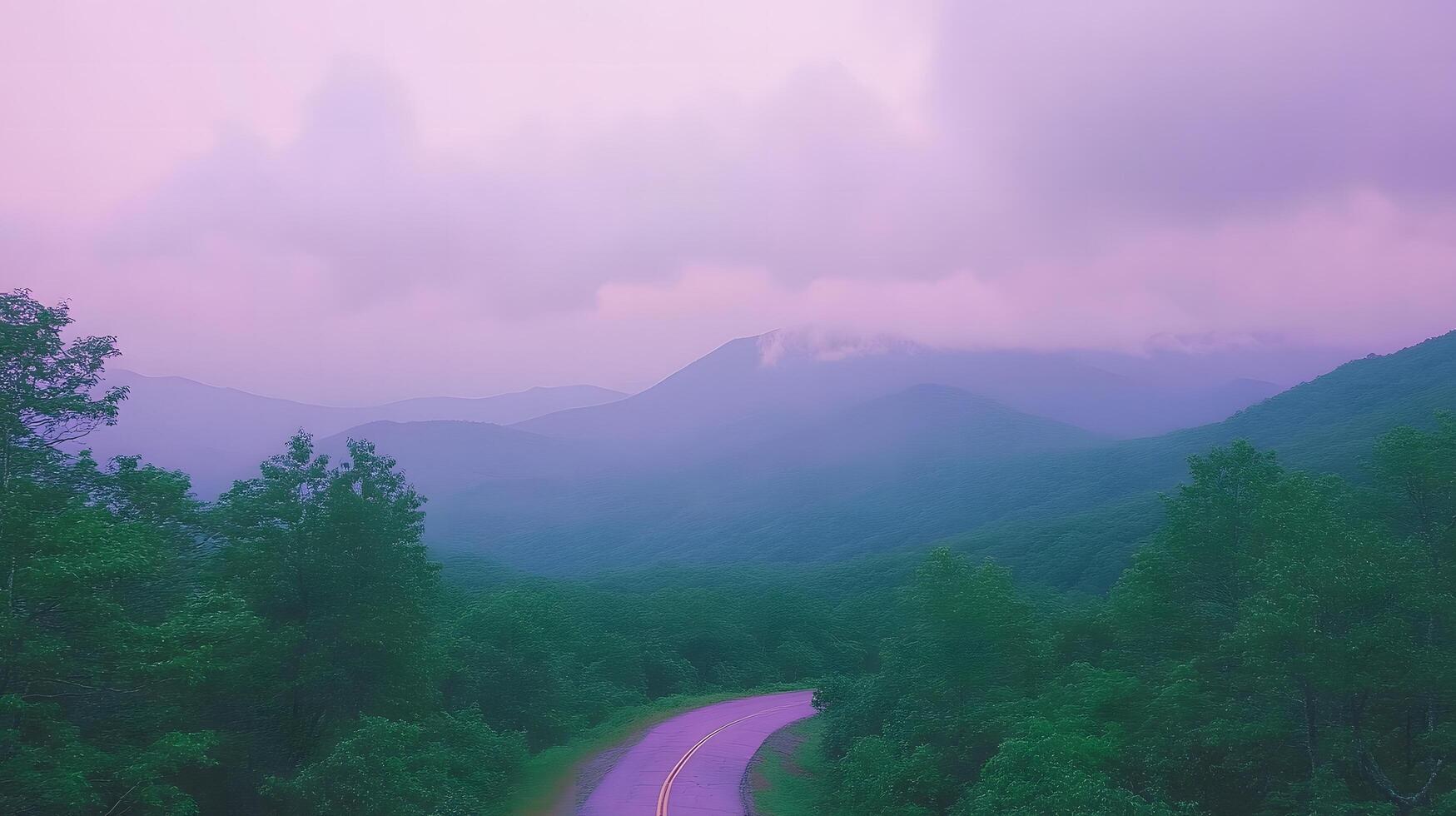 A scenic view of a road winding through lush green trees and mountains under a cloudy sky at dusk photo