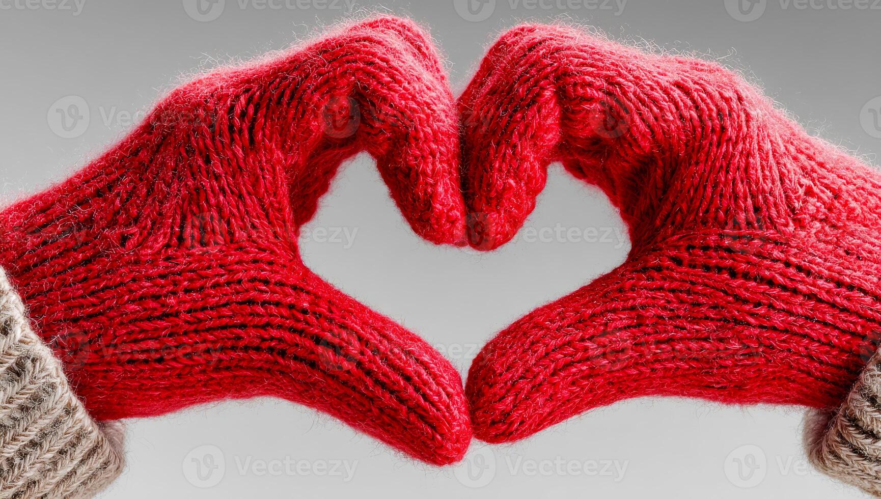 Hands in red gloves create a heart shape. Two hands wearing knitted red gloves form a heart shape against a neutral background, symbolizing warmth and affection. photo
