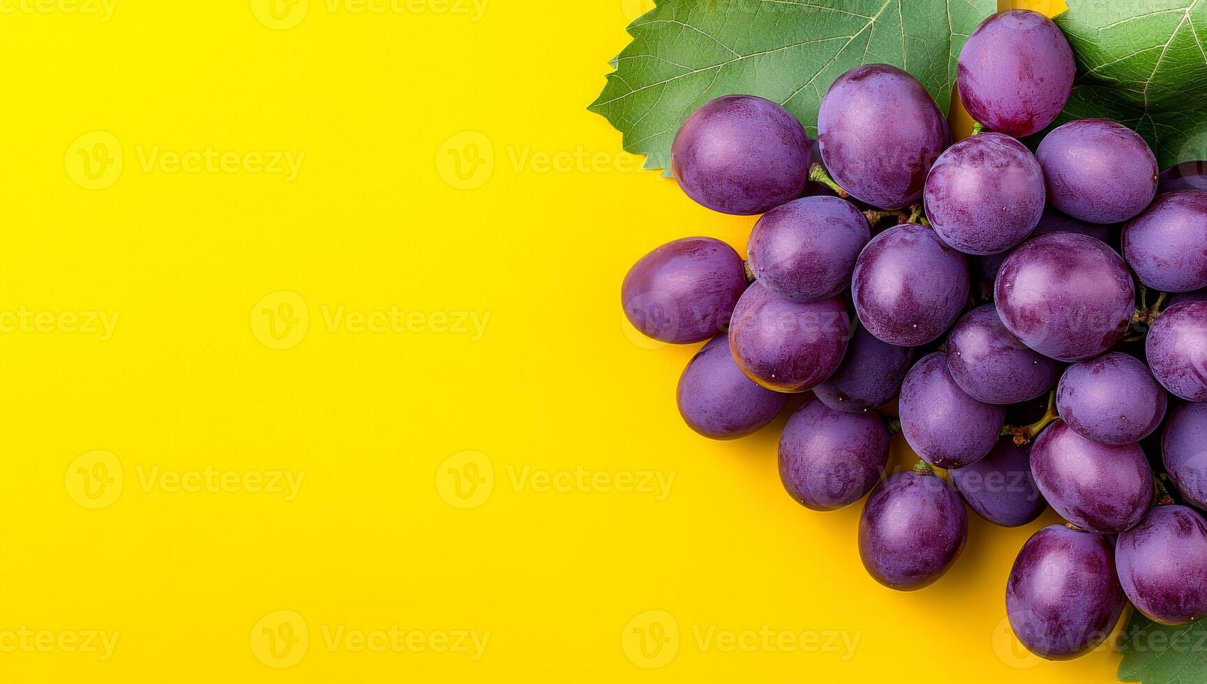 Vibrant purple grapes on bright. A bunch of ripe purple grapes rests on vibrant yellow, showcasing their glossy skin and green leaves. photo