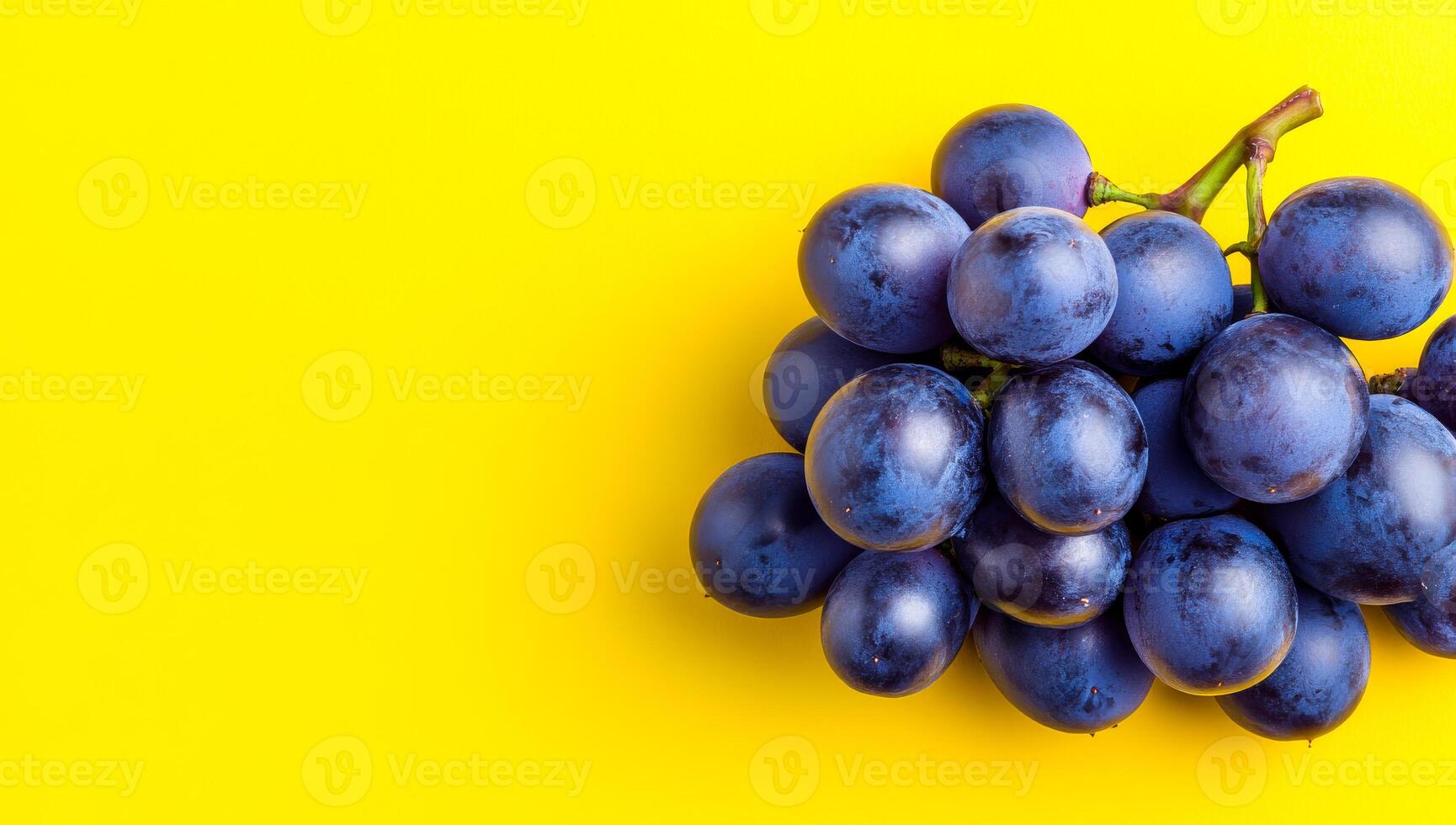 Grapes on yellow background. Bunch of dark purple grapes arranged on a vibrant yellow surface creating a striking visual contrast. photo