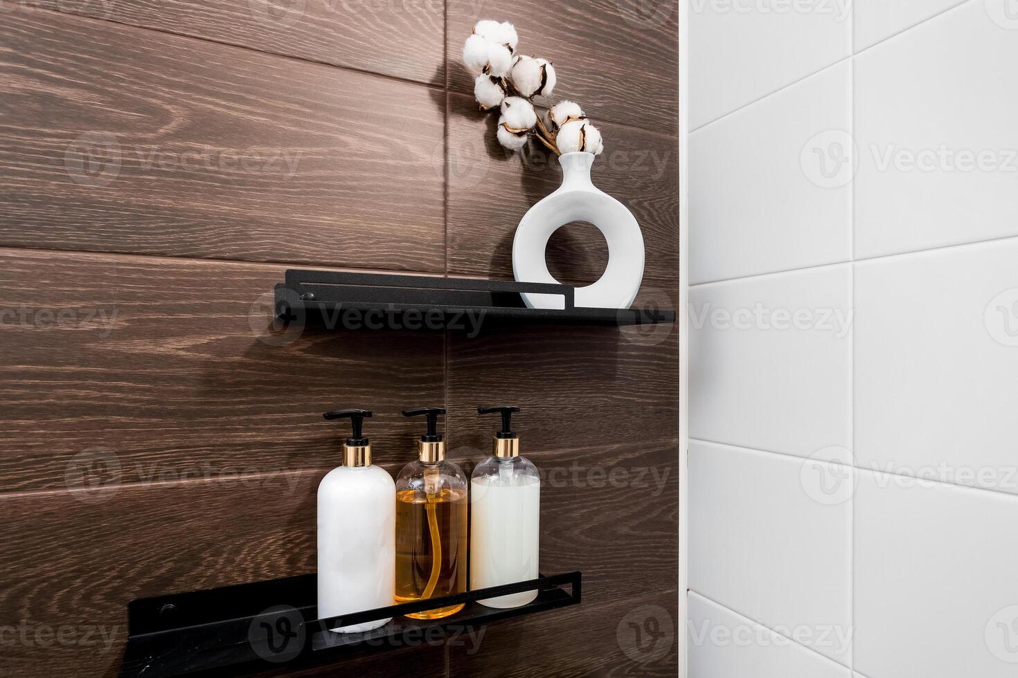 Accessories on black shelves a vase with cotton, bottles with dispensers, background brown tile with wood texture and white tile. photo