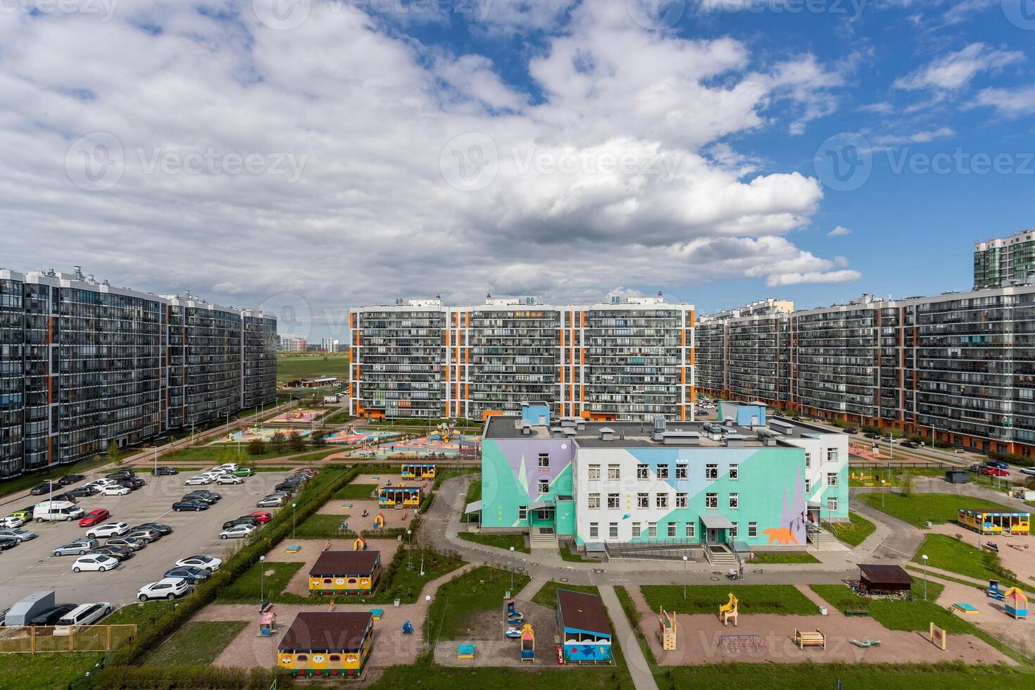 Modern residential complex with multi-story buildings, parking, and a bright kindergarten building with playgrounds. photo