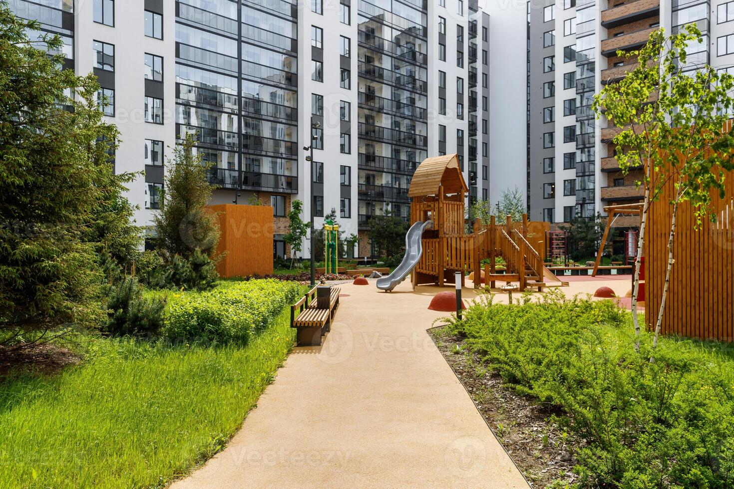 Landscaped courtyard with a wooden play complex, a path, and bushes against the background of multi-story buildings. photo