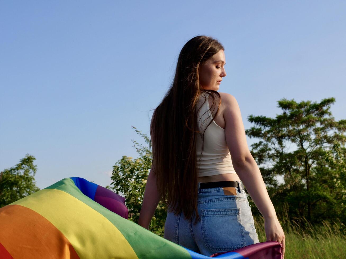 A woman holding a rainbow flag in the grass photo
