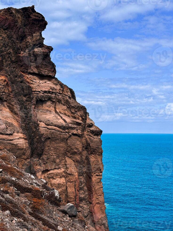 Madeira island Portugal composition of 3 elements earth geology hills cliff rocks blue water cloudy sky Atlantic Ocean shore seascape rough mountains scenery vacation hiking trail vertical photography photo