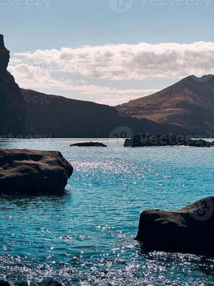 Madeira island Portugal no people rocks blue water sun beams reflection Atlantic Ocean shore seascape rough cliff hill mountains scenery vacation idyllic tranquility vertical photography color image photo